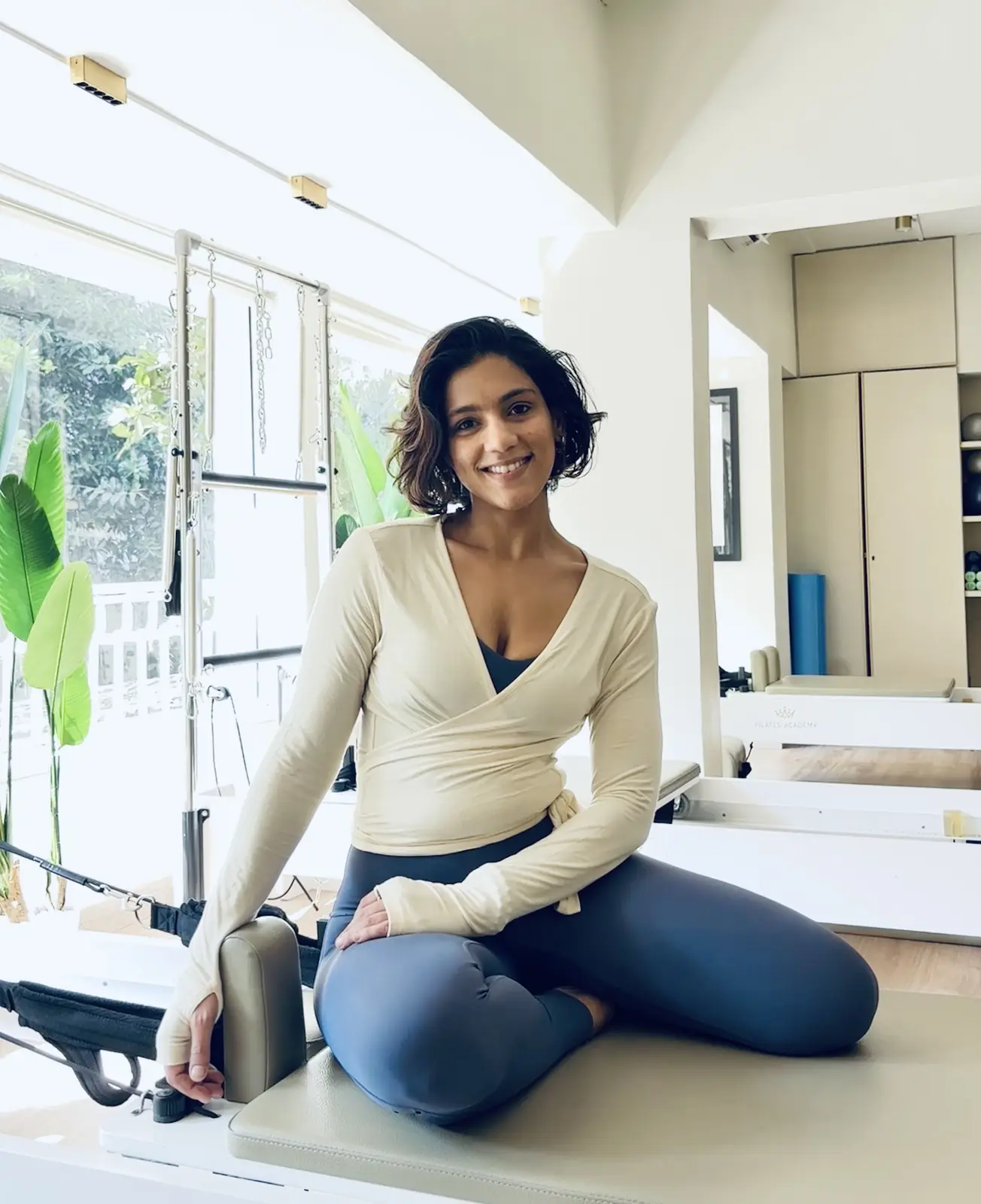 Divya smiling, seated on a Reformer